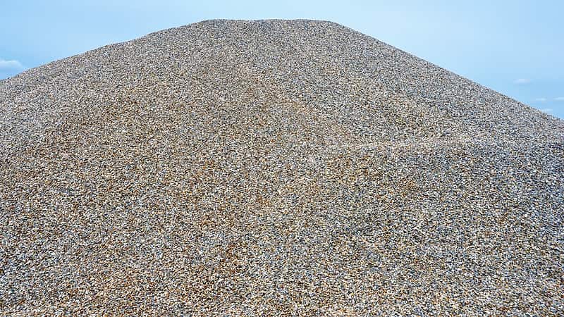 A front loader filling a haul truck from a graded stockpile of washed gravel at a pit cut into a dry river terrace.