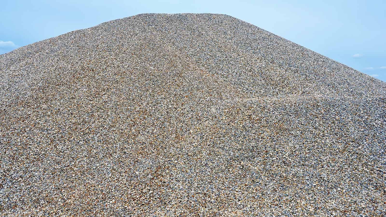 A front loader filling a haul truck from a graded stockpile of washed gravel at a pit cut into a dry river terrace.