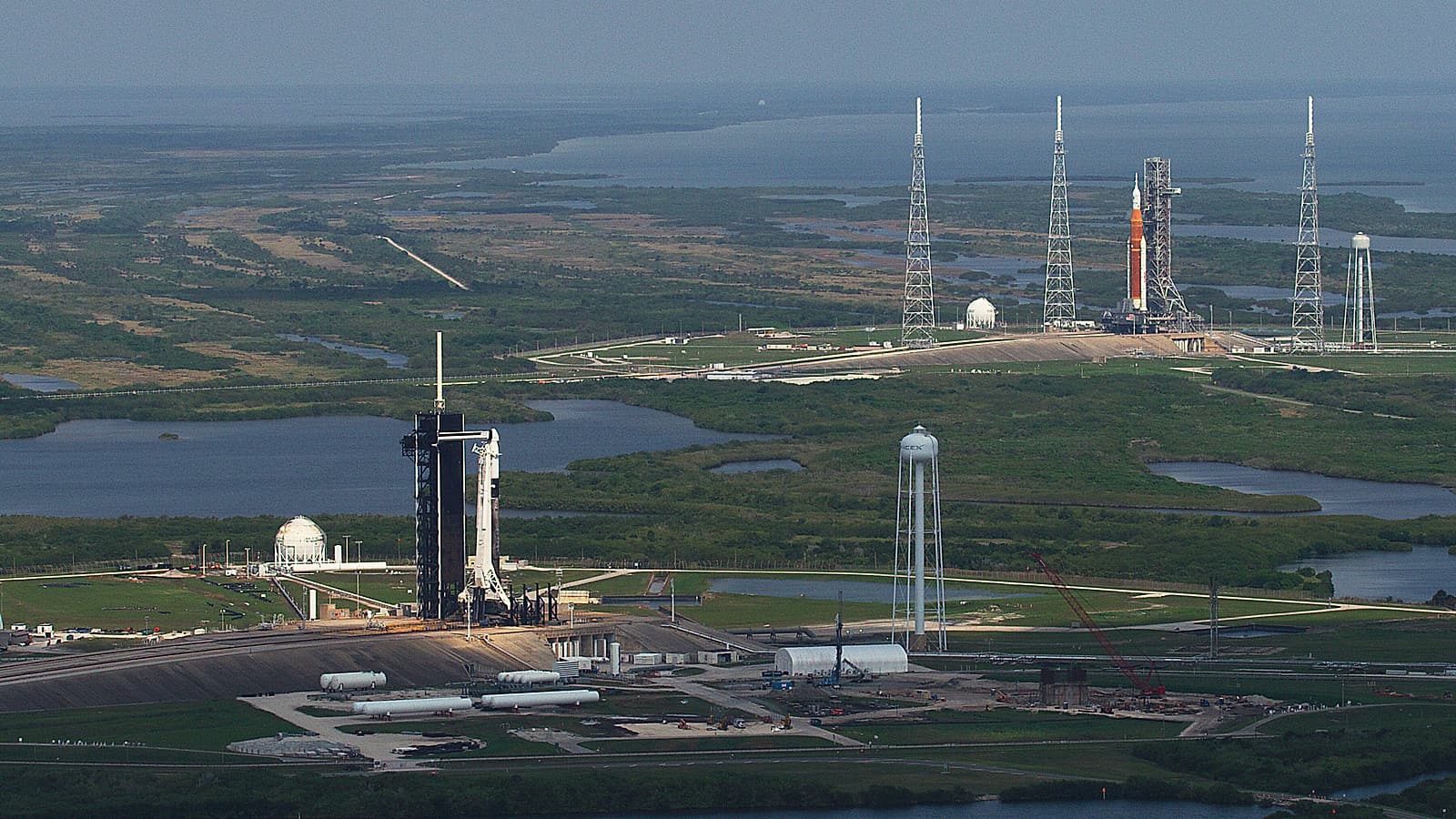 A tall white rocket standing against a metal service tower at dawn with vapor drifting from its side.